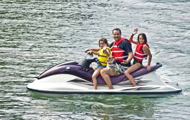 Father and daughters waving from jet ski